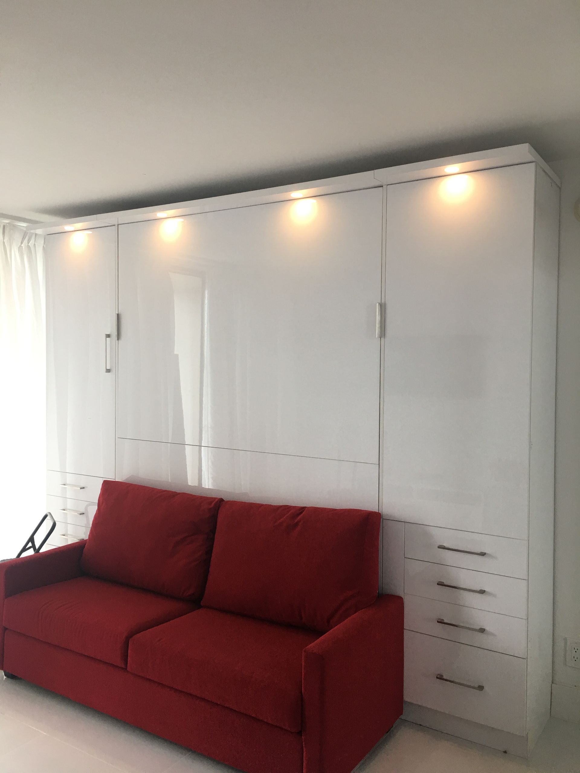 A red couch is sitting in front of a wall of white cabinets