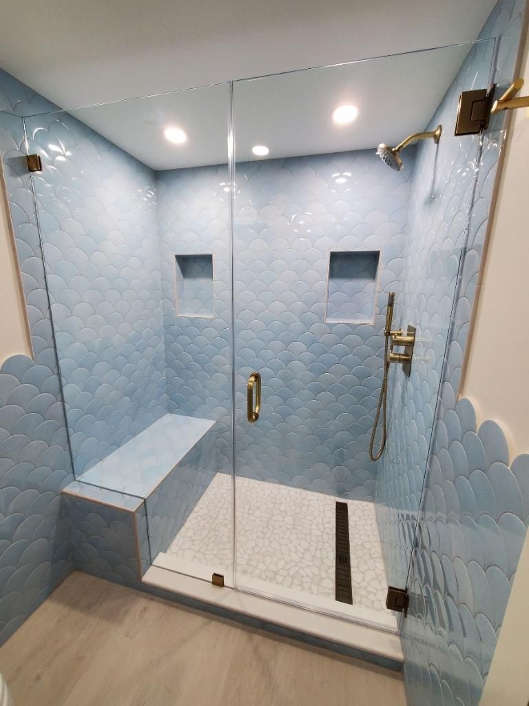 A bathroom with blue tiles and a walk in shower with a glass door.