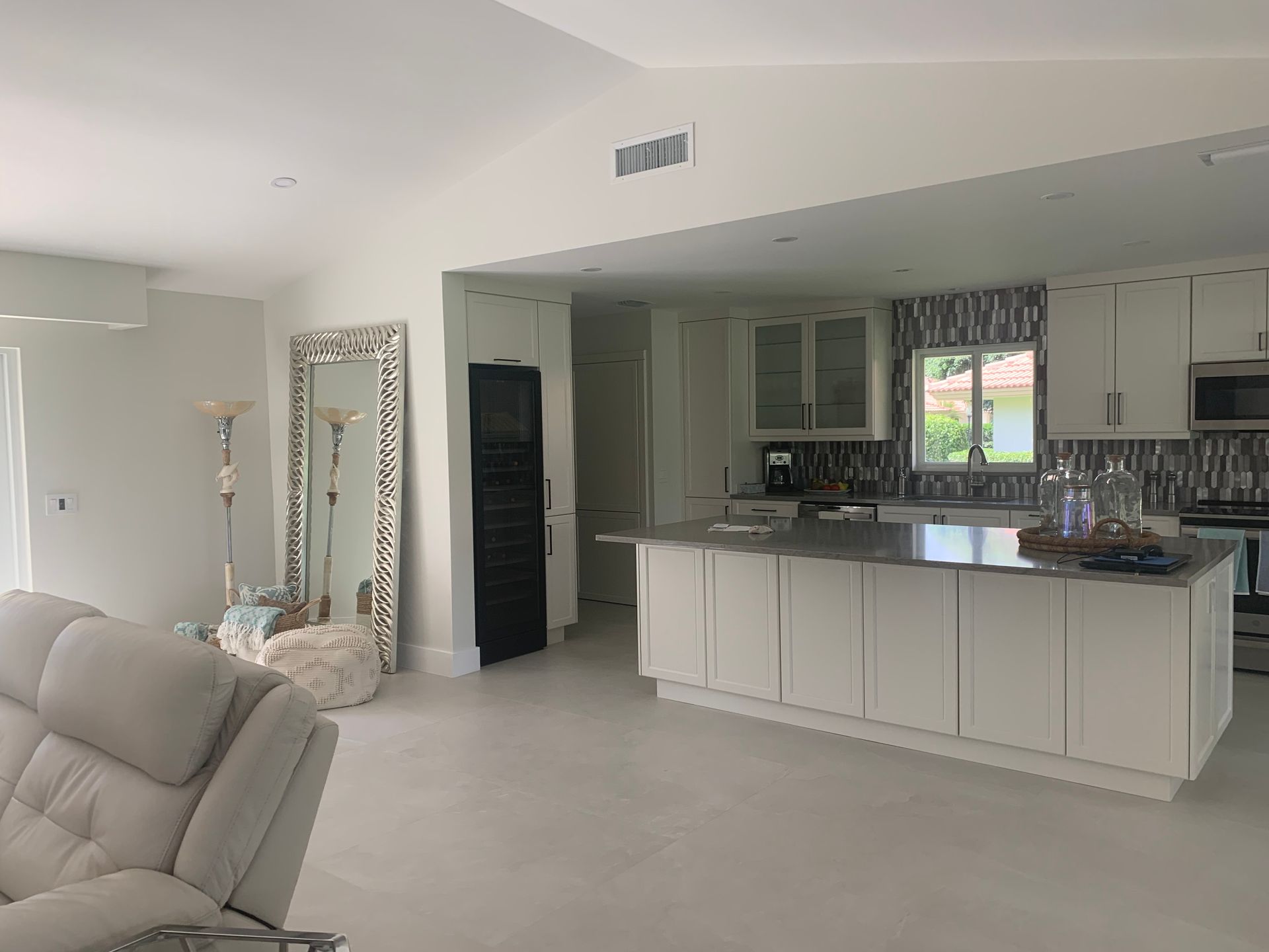 A living room filled with furniture and a kitchen with a large mirror.
