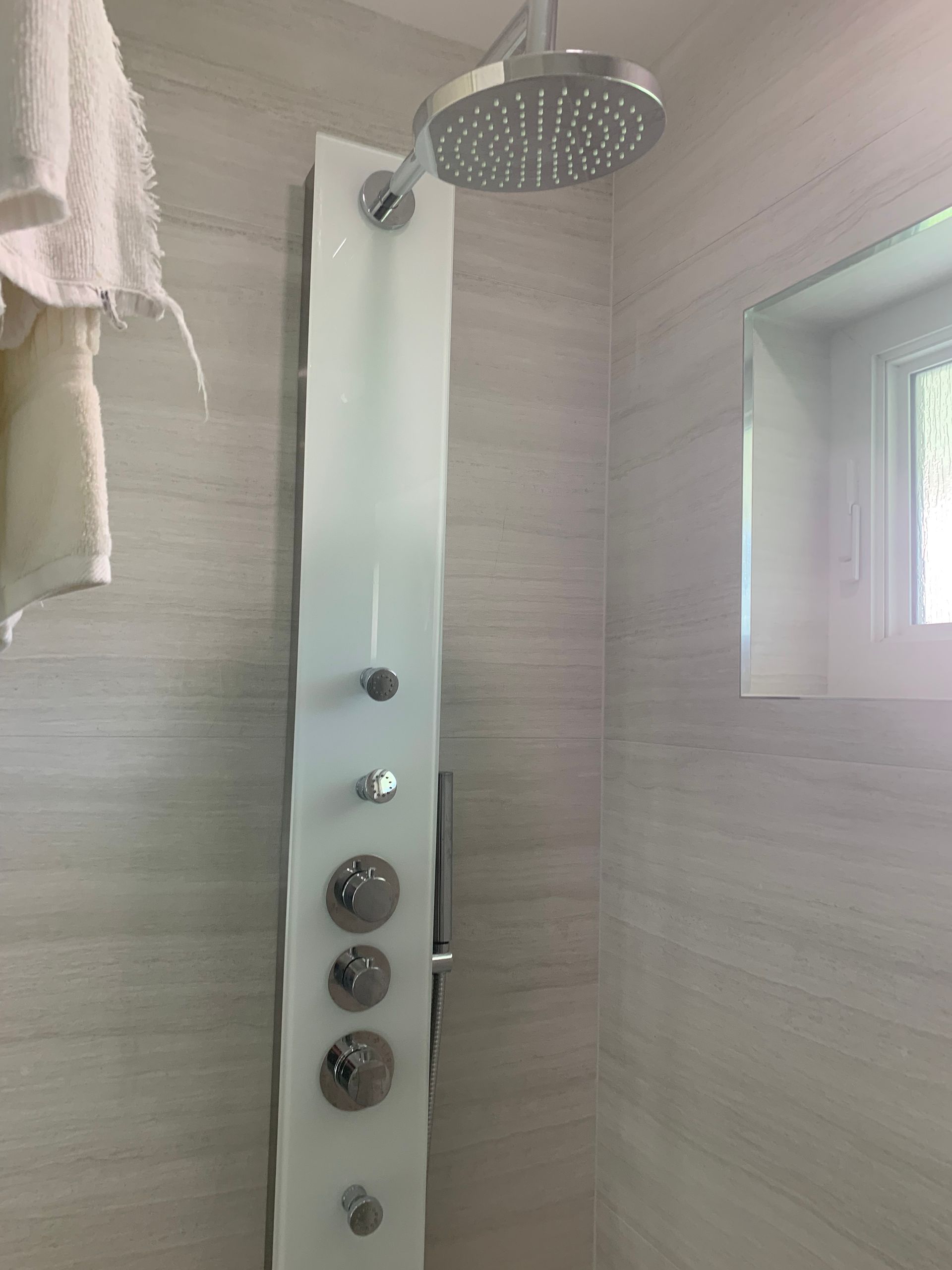 A shower head is hanging from the ceiling in a bathroom next to a window.