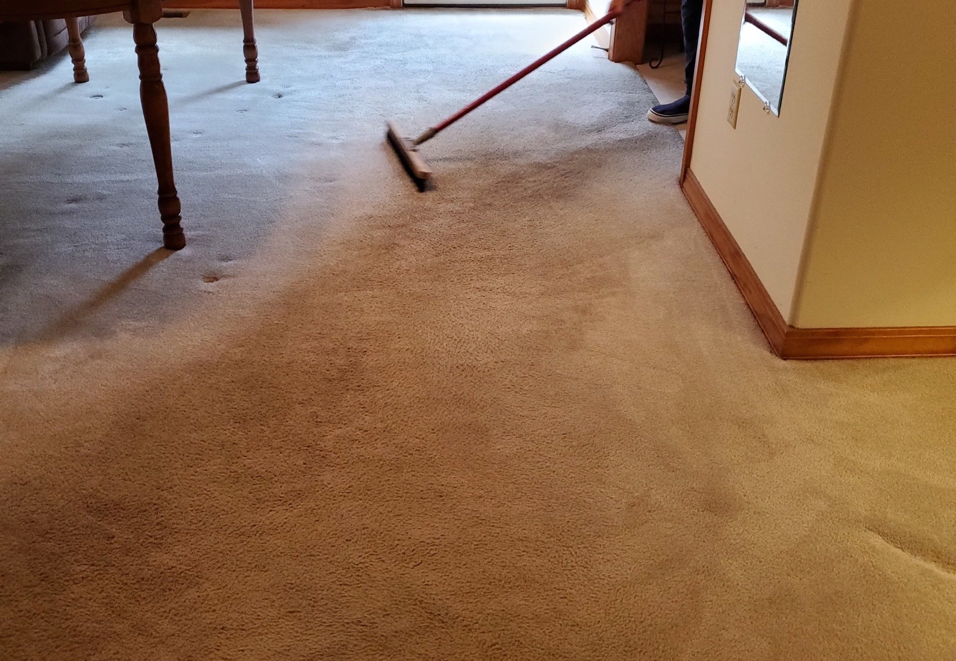 A person is sweeping a carpet with a broom in a living room.