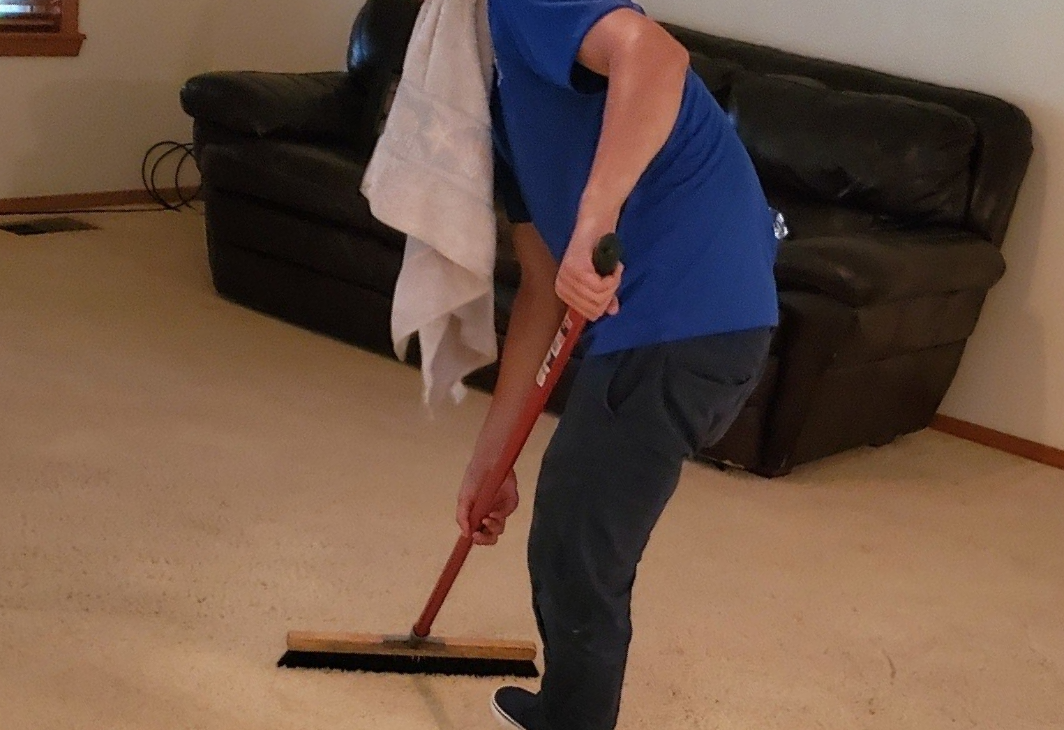 A man in a blue shirt is cleaning the floor with a broom.