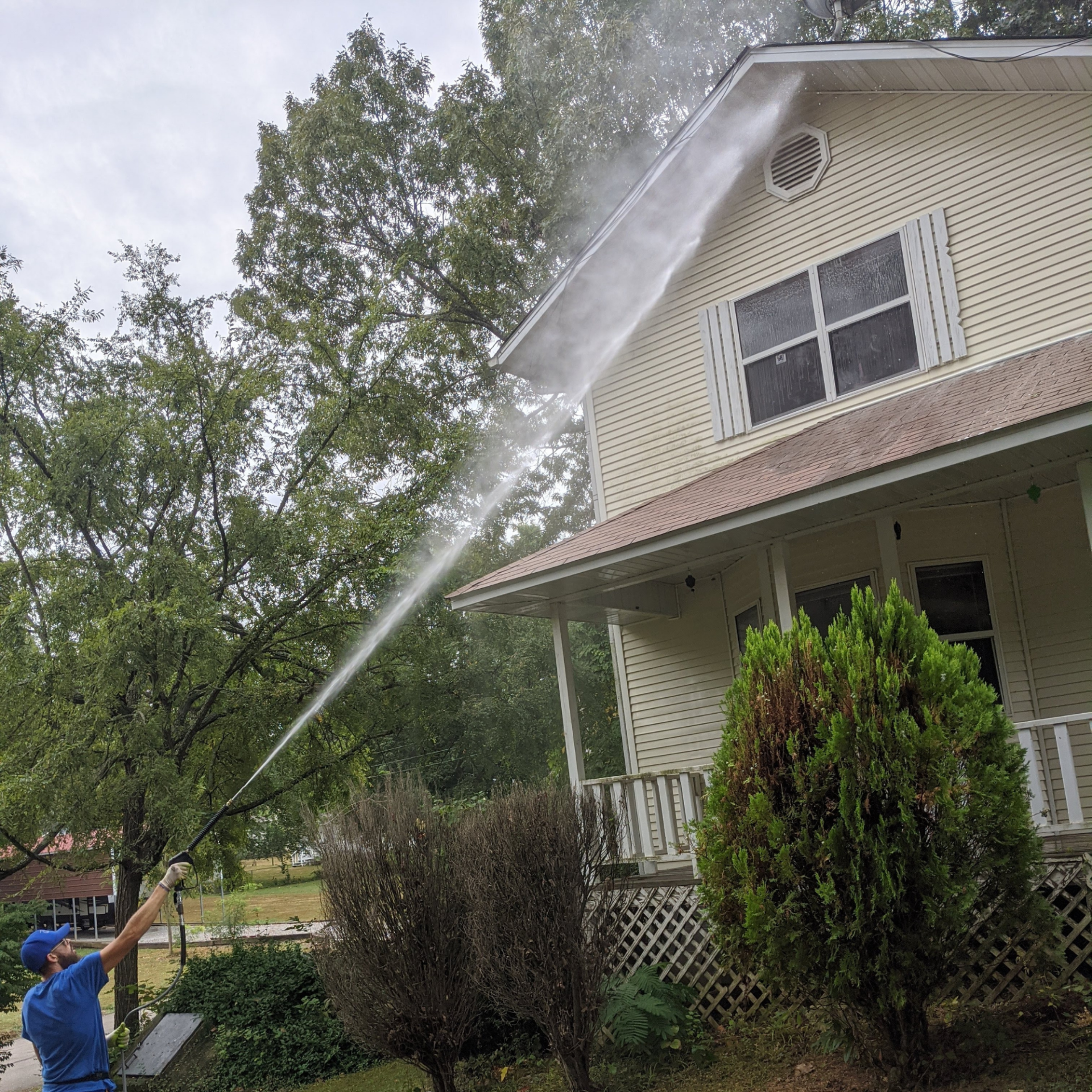 A man is using a high pressure washer to clean the side of a house.