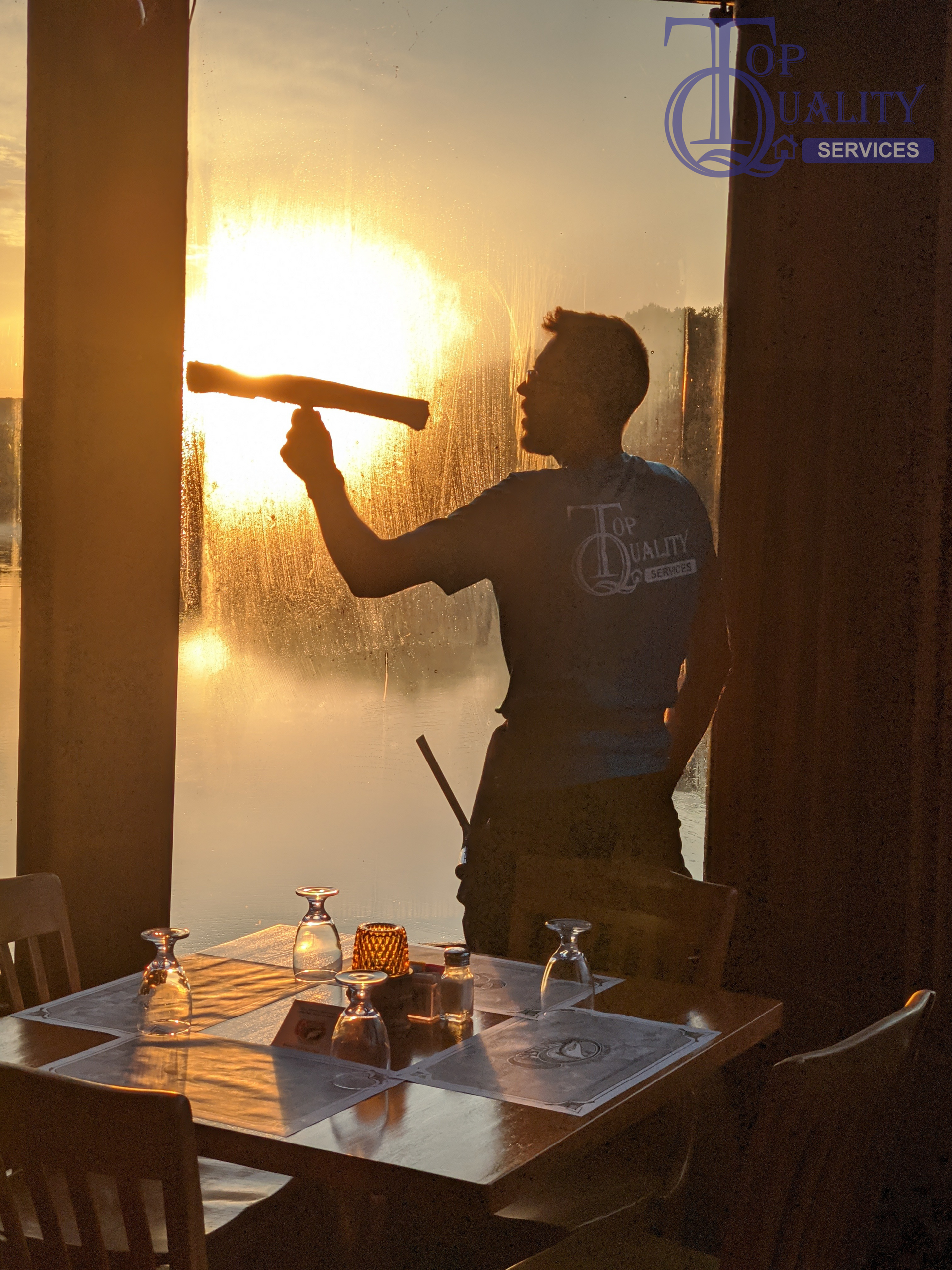 A man is cleaning a window in a restaurant at sunset
