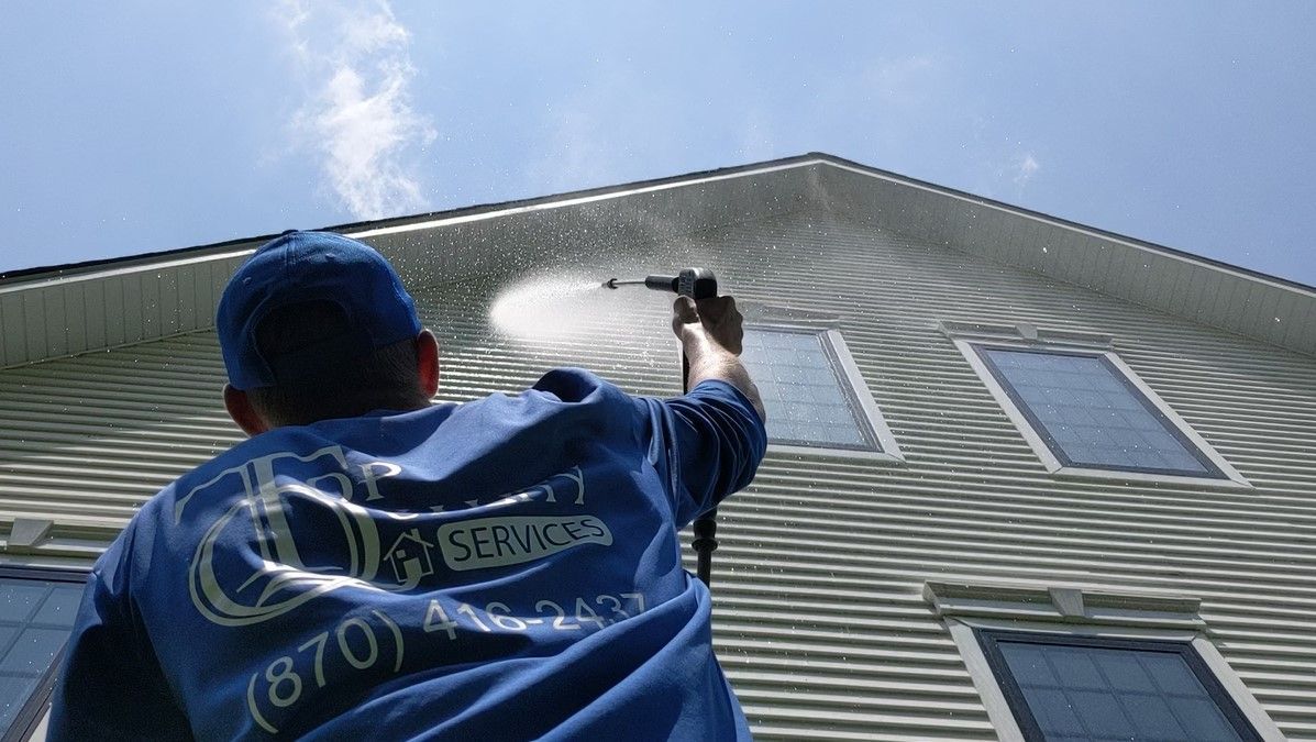 A man is cleaning the side of a house with a pressure washer.