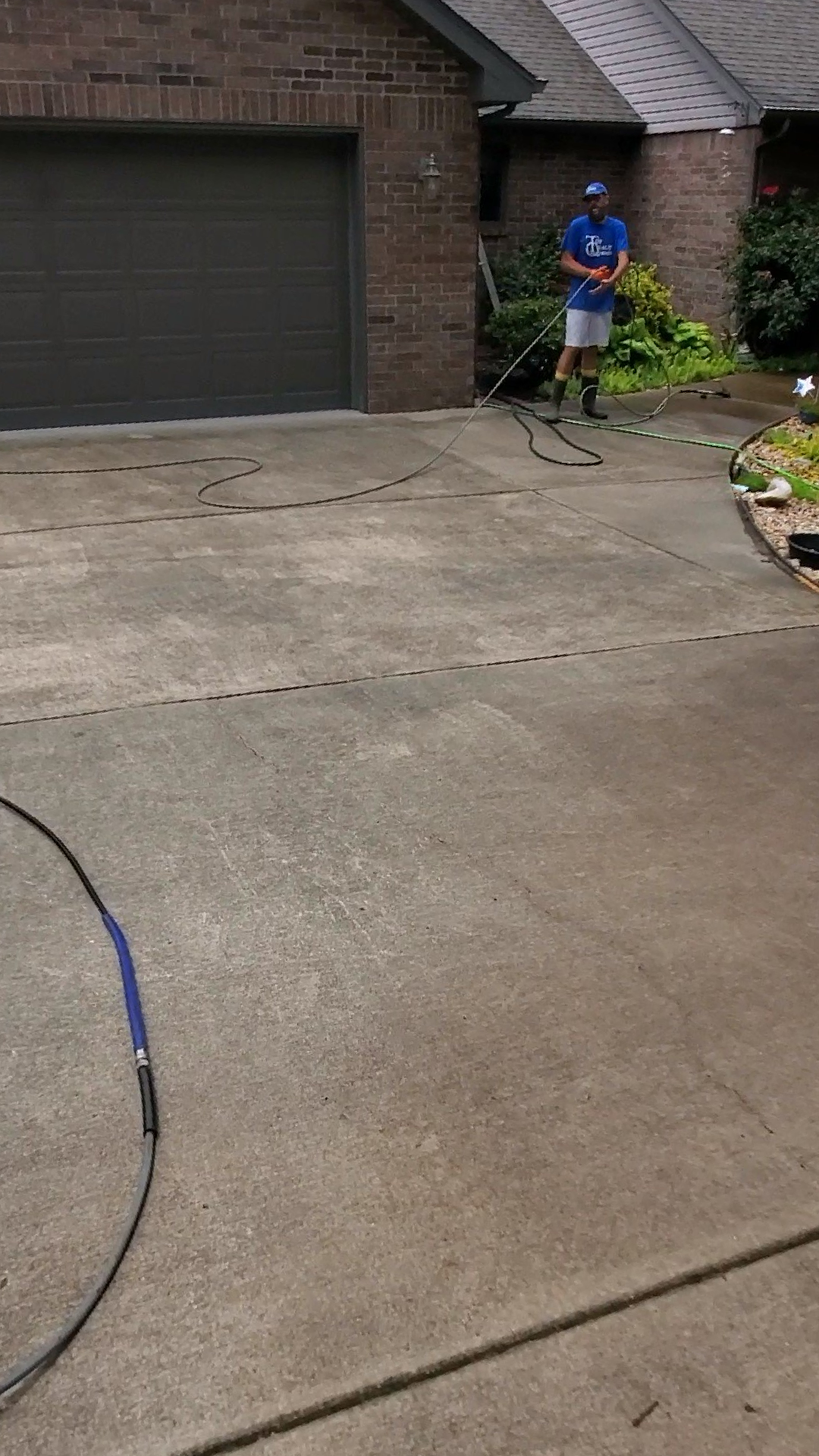 A man is using a pressure washer to clean a driveway in front of a house.