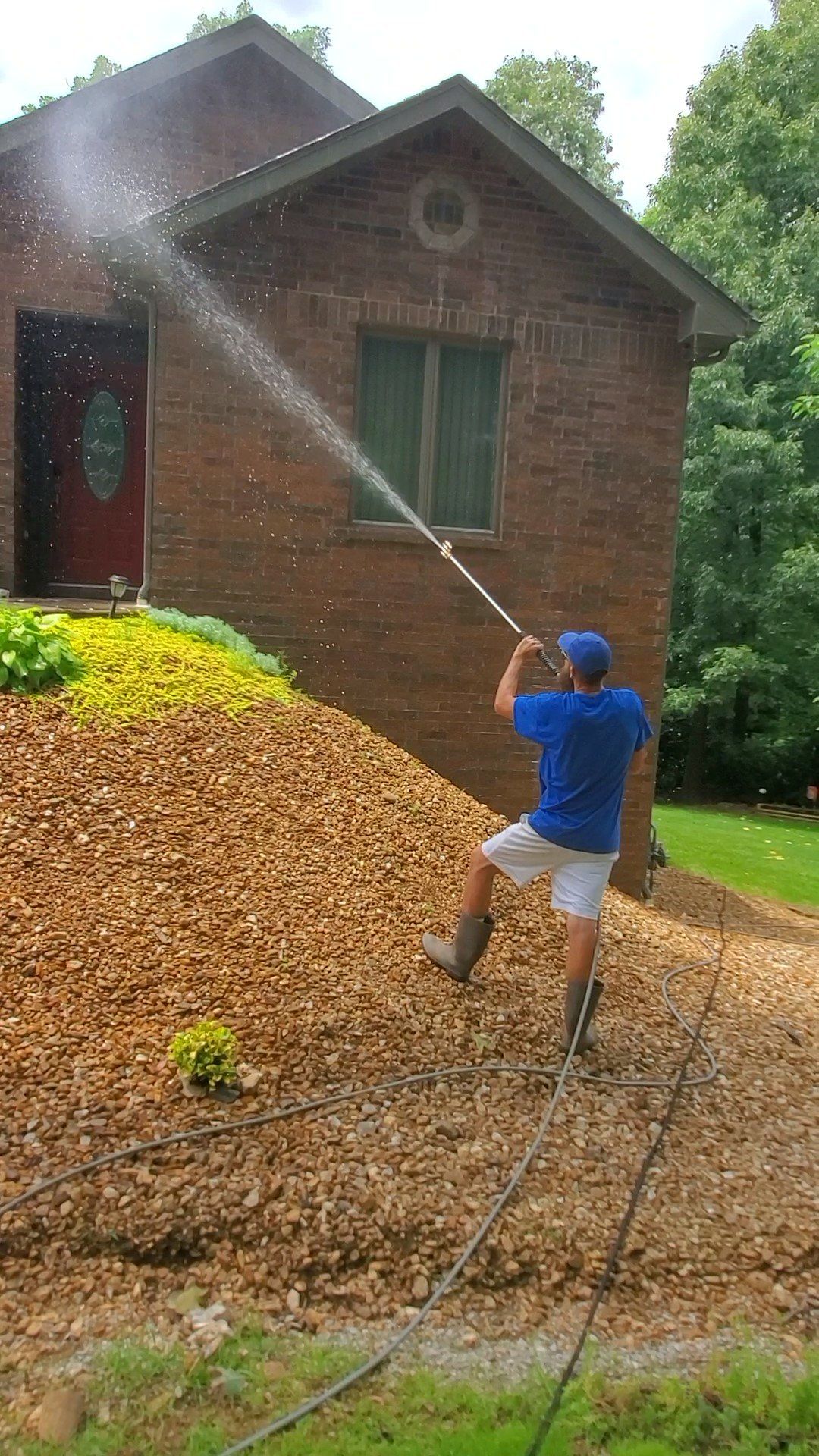 A man is using a high pressure washer to clean the sidewalk in front of a brick house.