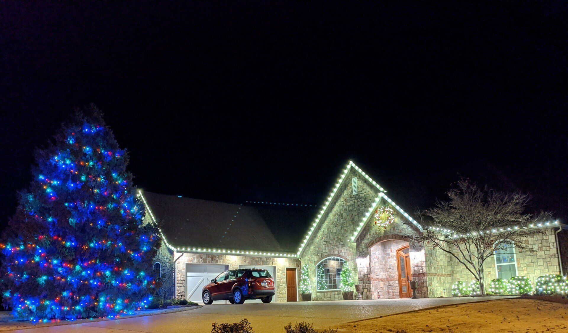 multi-color Christmas lights and a residential house with a hung wreath and custom lights put up by top quality home services