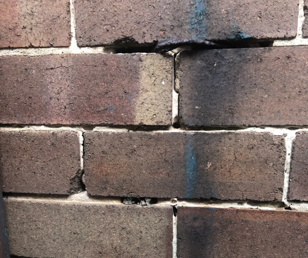 Close-up of a brick wall with black soot staining around a vertical crack and mortar joints