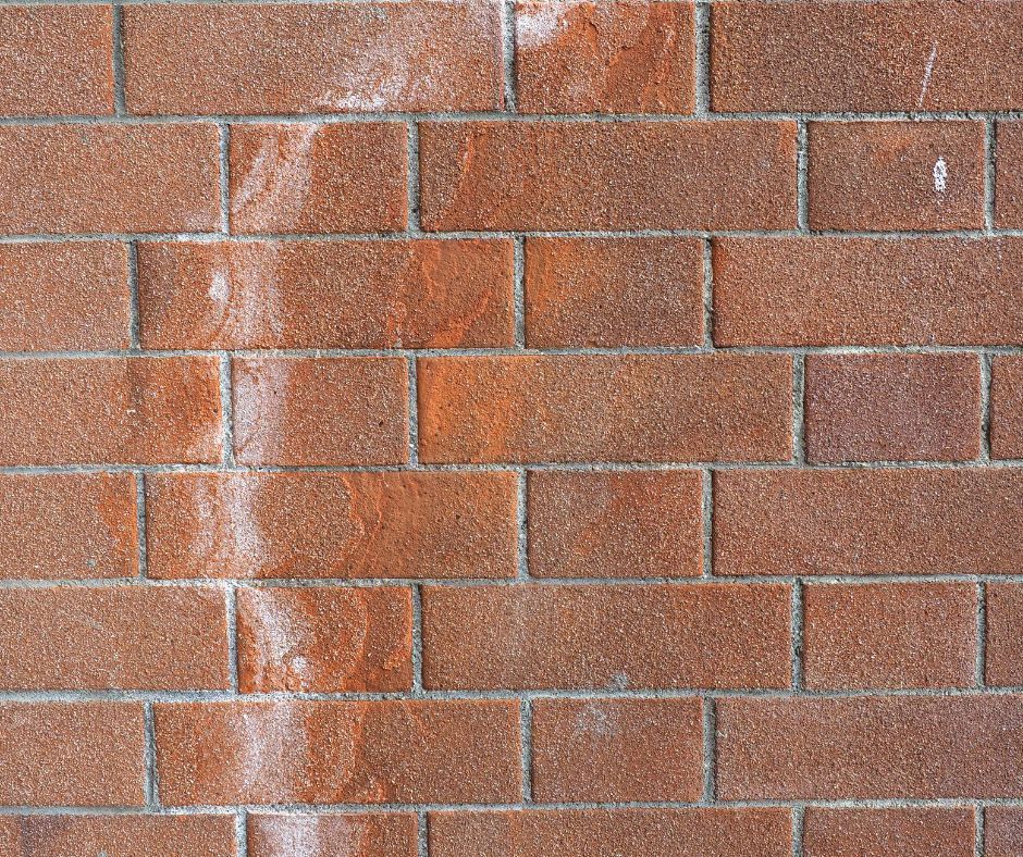 Close-up of a weathered red brick wall with white streaks of crystalline salts on the surface.