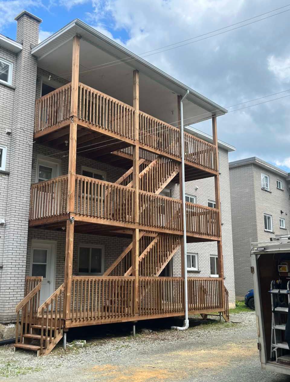 Une structure en bois de trois étages comprenant un balcon et un escalier, adossée au côté d'un immeuble résidentiel en briques.