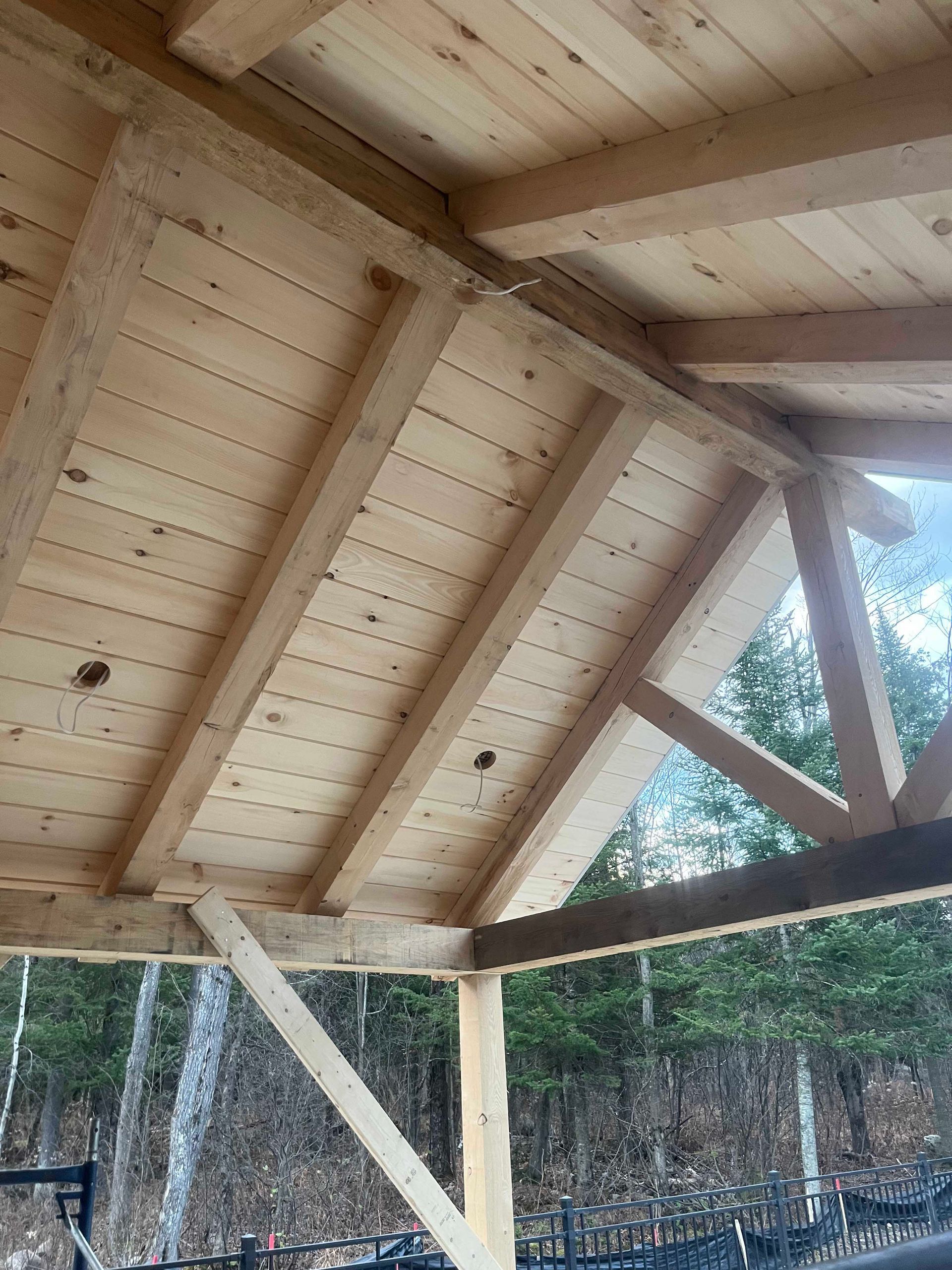 Vue en contre-plongée d'une structure de toit de gazebo en bois inachevée, avec des chevrons apparents et un platelage en pin à rainure et languette.