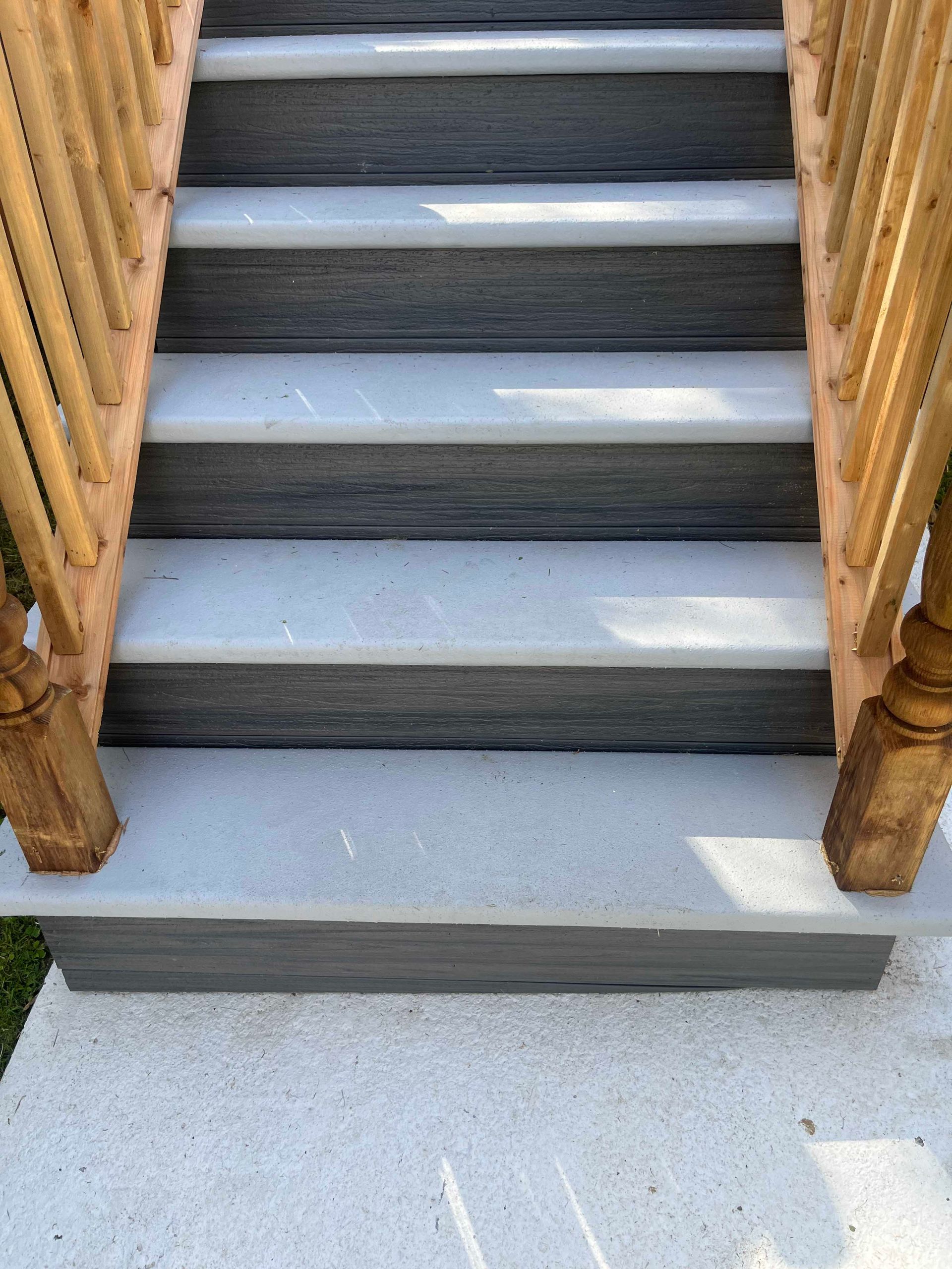 Un escalier extérieur avec des marches texturées gris clair et des contremarches gris foncé, flanqué de rampes en bois.