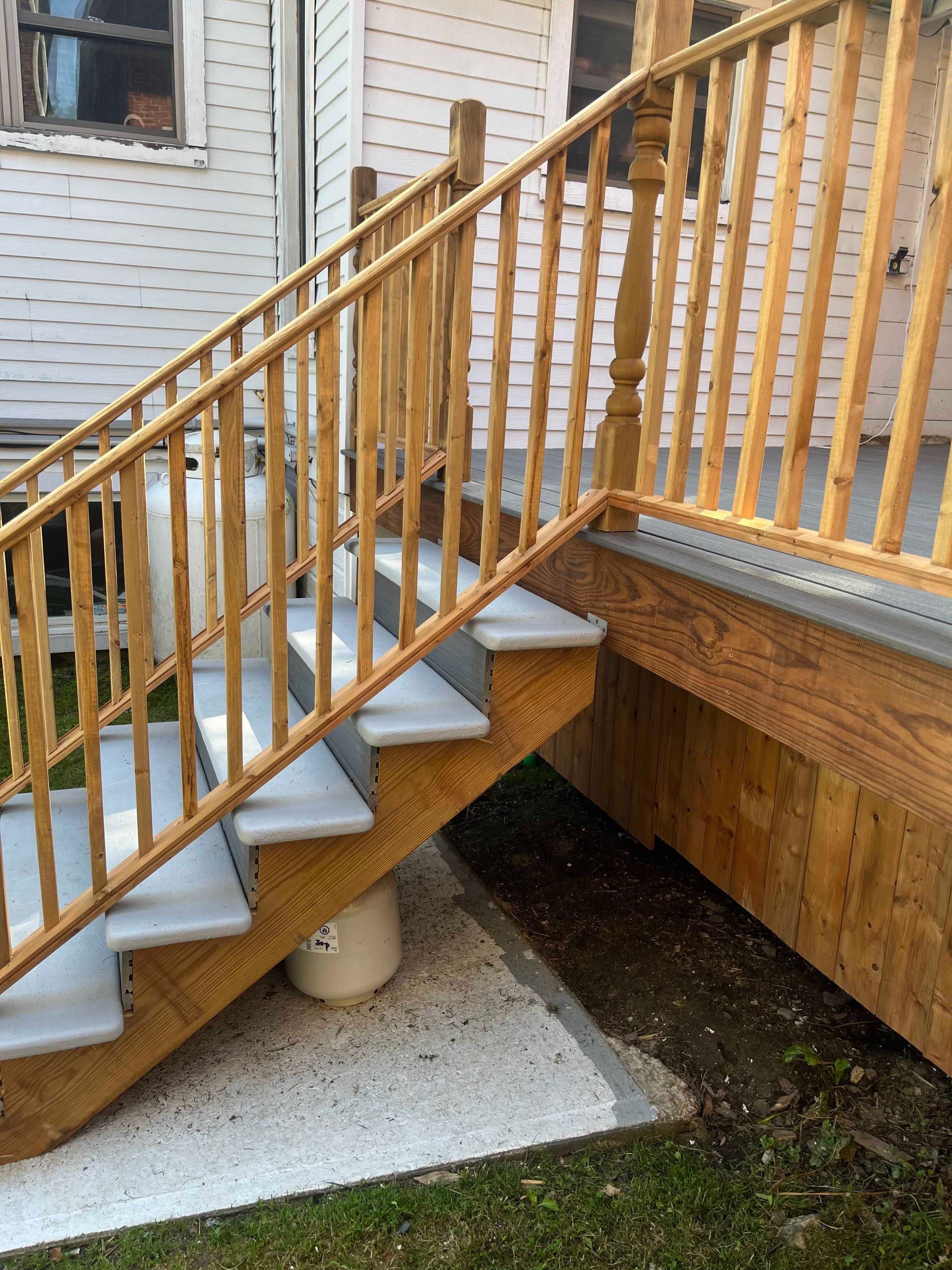 Escalier extérieur avec marches grises et rampes en bois menant à un porche, situé contre une maison à façade claire.