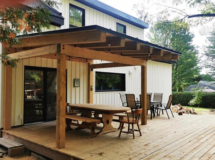 Une terrasse en bois avec un patio couvert comprenant une table et des chaises, adossée à une maison de couleur claire.