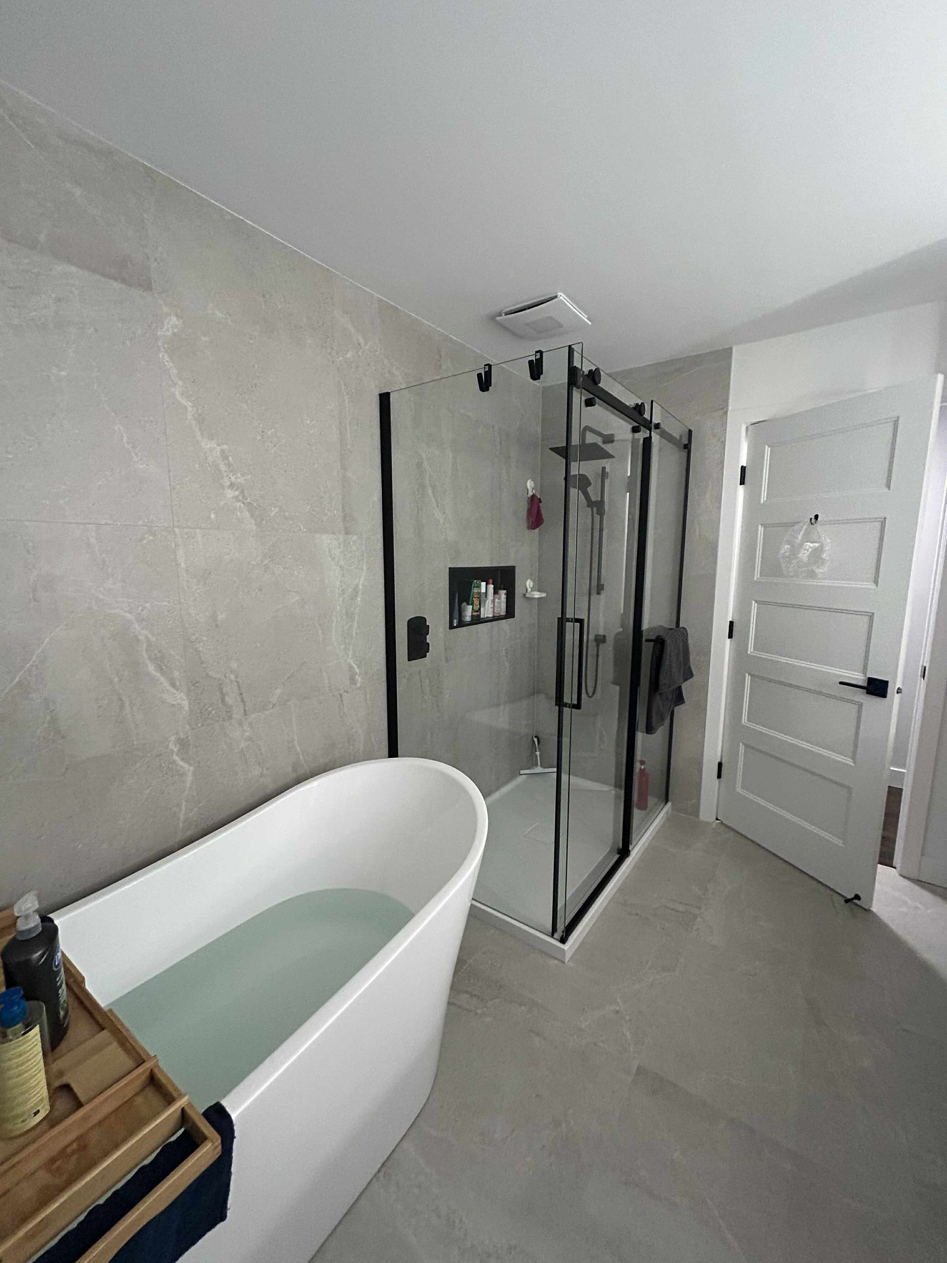 Une salle de bains moderne avec une baignoire îlot blanche, une douche à l'italienne et des murs et sols carrelés gris clair.