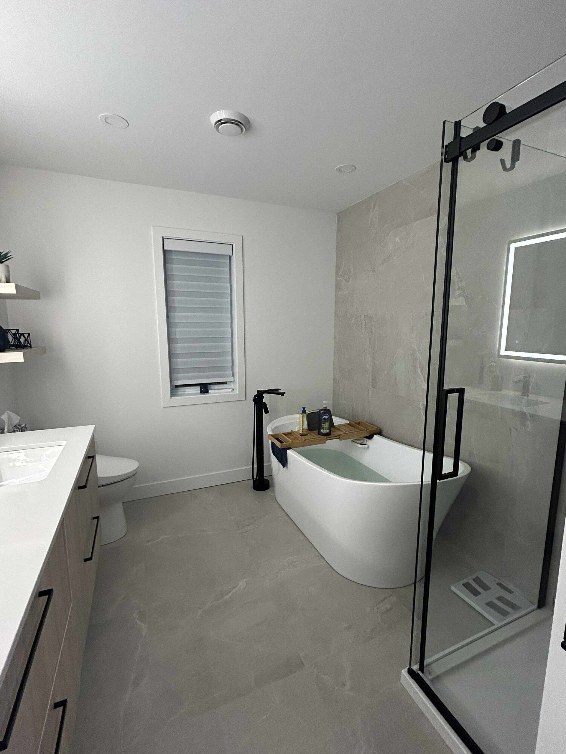 Salle de bains moderne avec baignoire blanche, douche vitrée, double vasque et carrelage gris au sol.