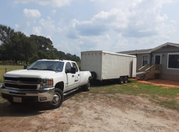 A white truck with a trailer attached to it is parked in front of a house.