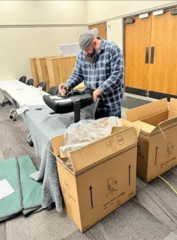 A man is packing a chair in a cardboard box.