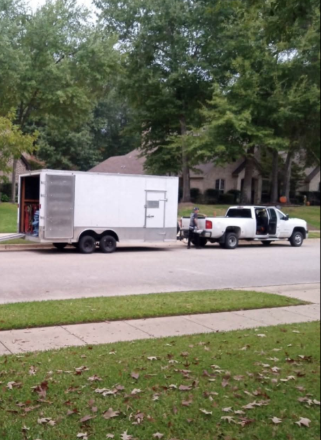 A white truck is pulling a white trailer down a street