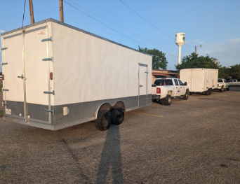 A row of white trailers are parked in a parking lot