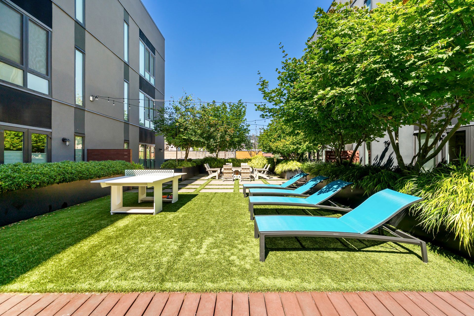 A lawn with blue lounge chairs and a ping pong table in front of a building.
