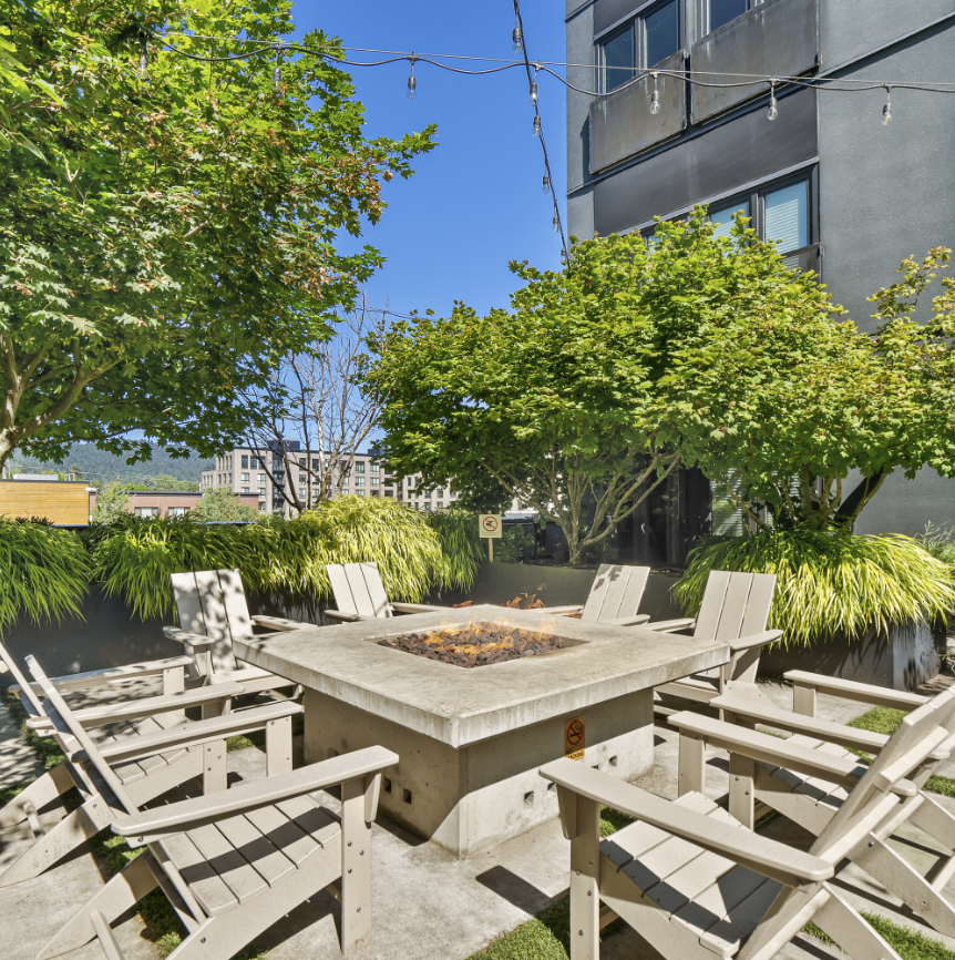 A patio with a fire pit and chairs in front of a building