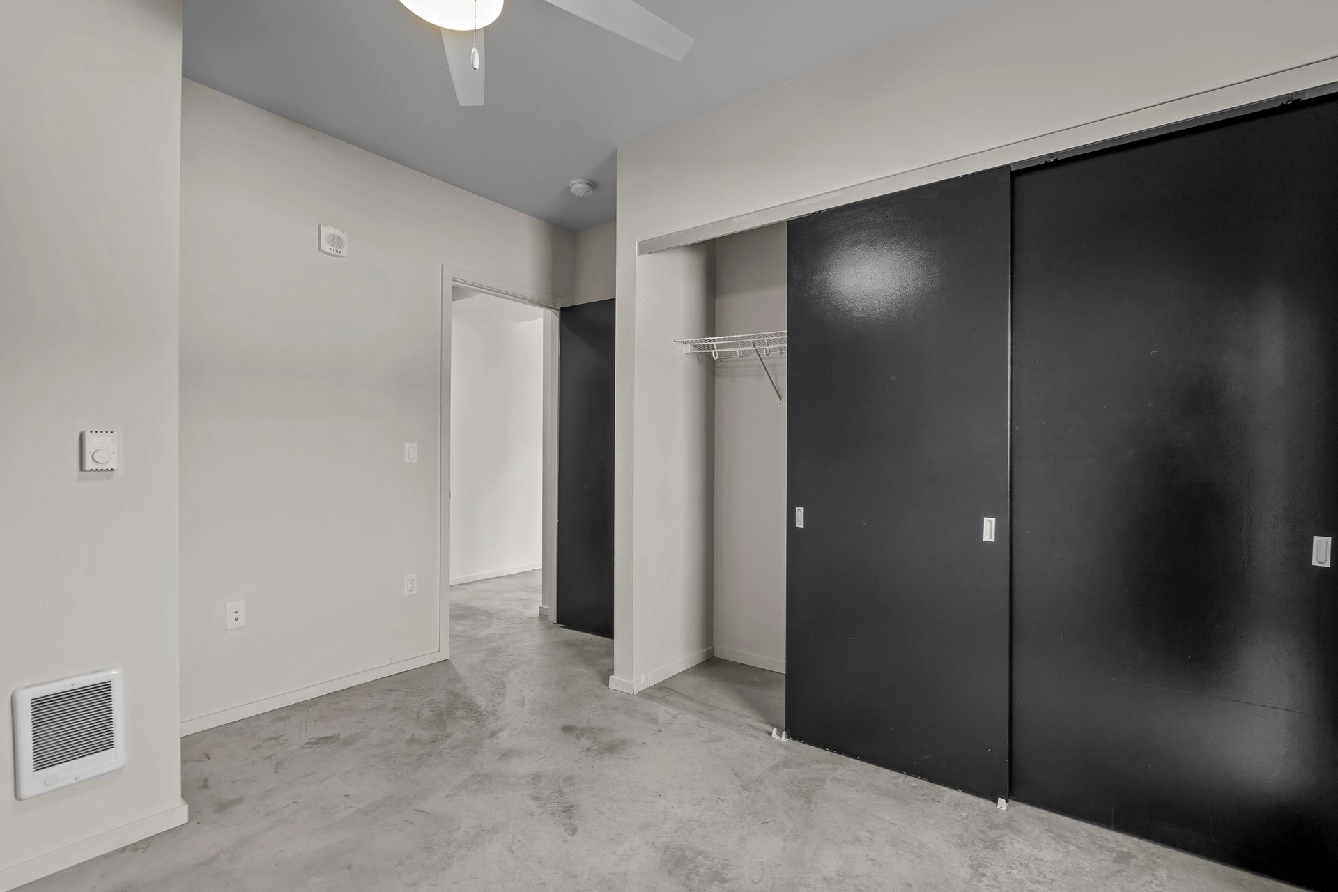 An empty bedroom with black sliding doors and a ceiling fan.