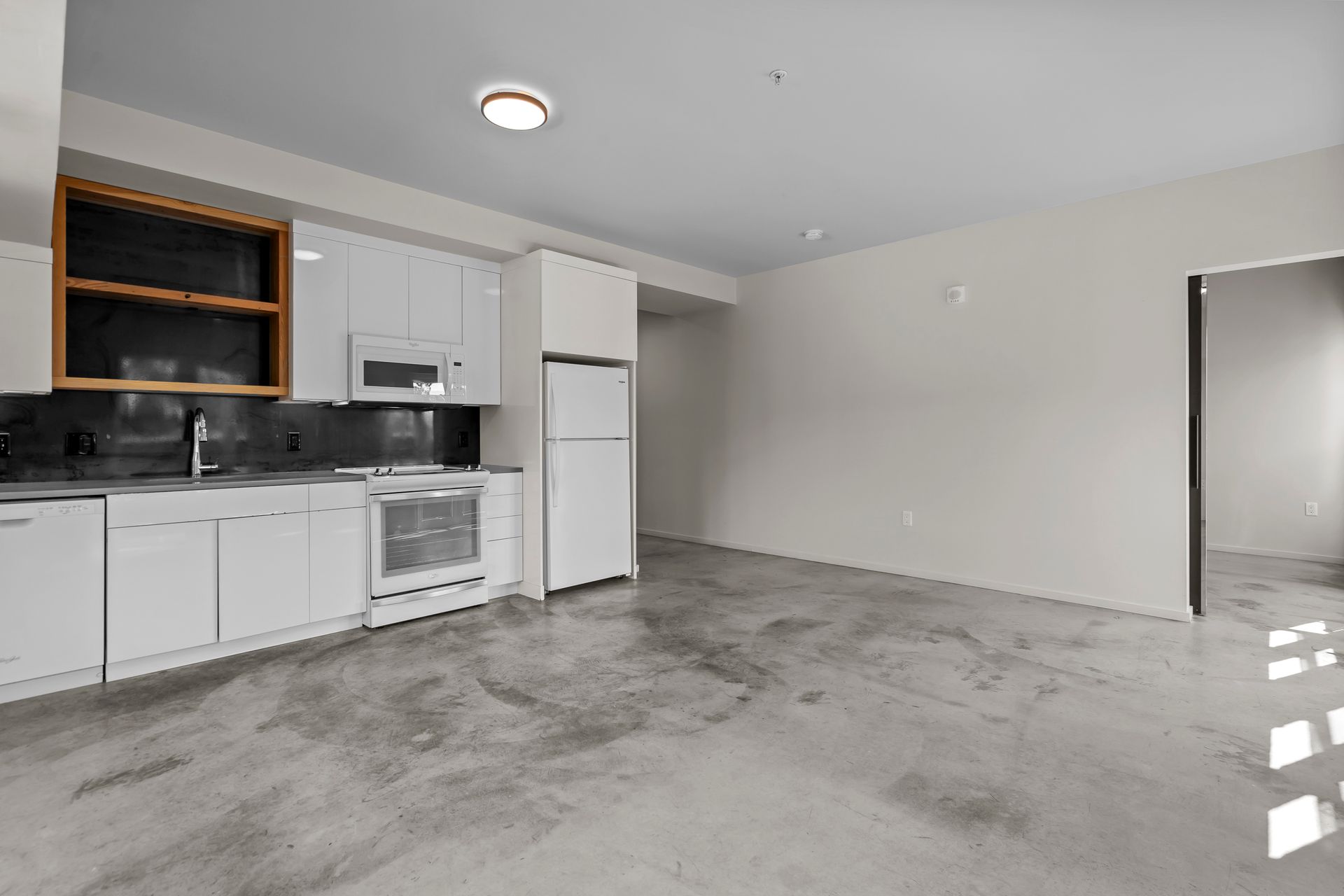 An empty kitchen with white cabinets and a concrete floor.