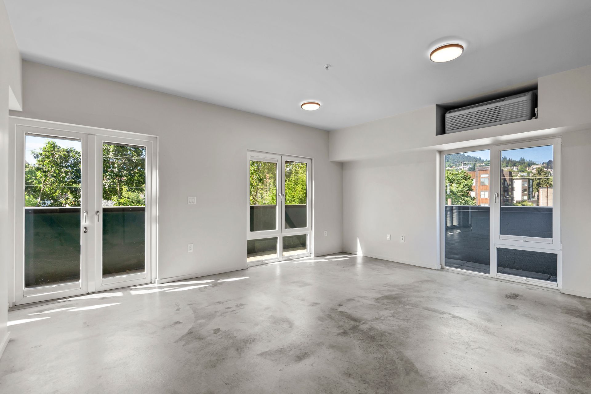 An empty living room with a balcony and sliding glass doors.