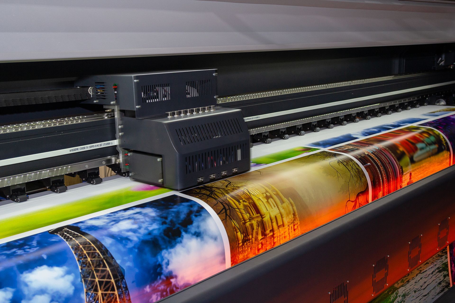 Large-format printer in operation, printing a colorful graphic on a roll of paper.