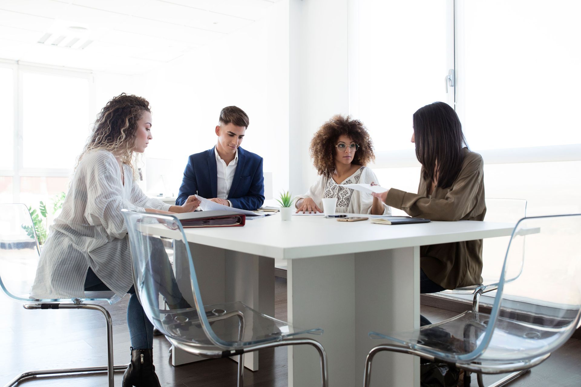 Four people in a bright room sit at a white table, reviewing documents.