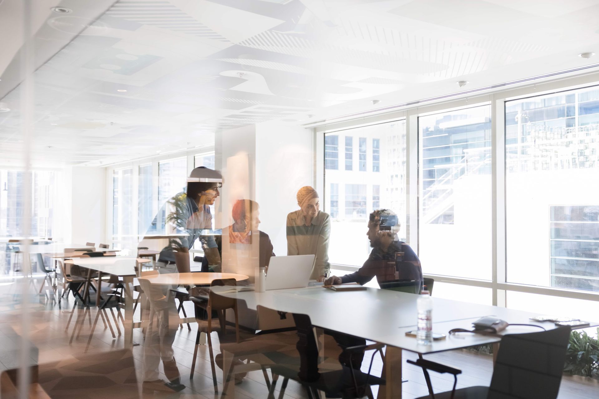 People in a bright office at a long table. They are looking at a laptop and chatting.