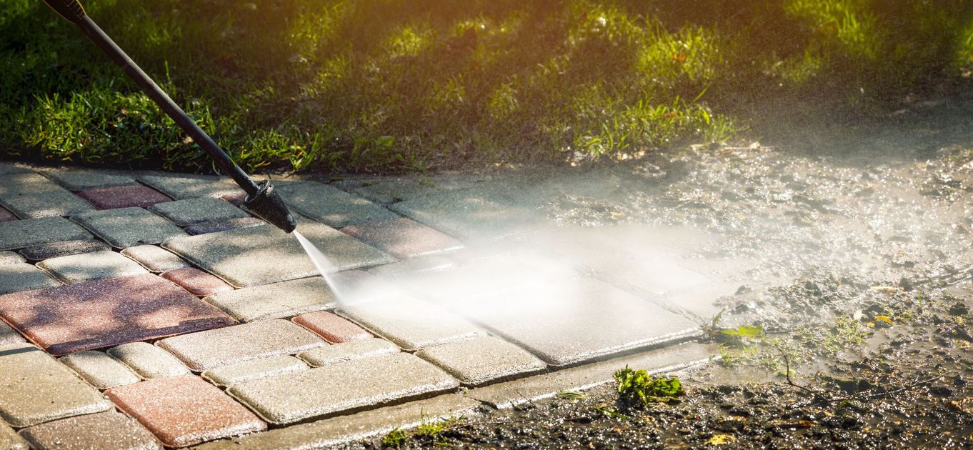 A person is using a high pressure washer to clean a brick walkway.