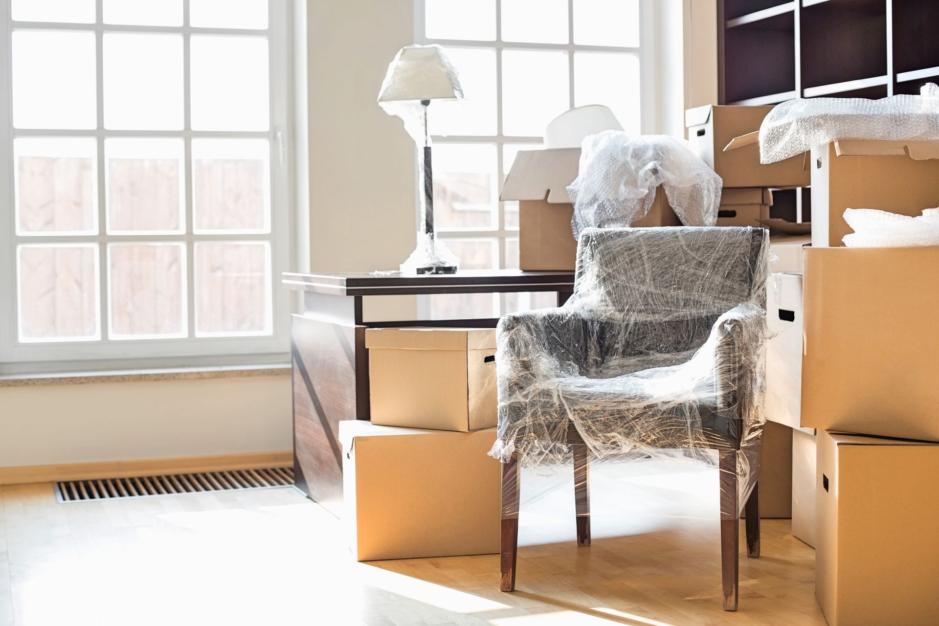 A chair is wrapped in plastic in a room filled with cardboard boxes.