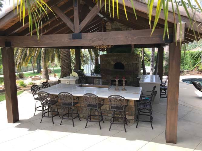A large outdoor kitchen with a wooden roof and a pizza oven