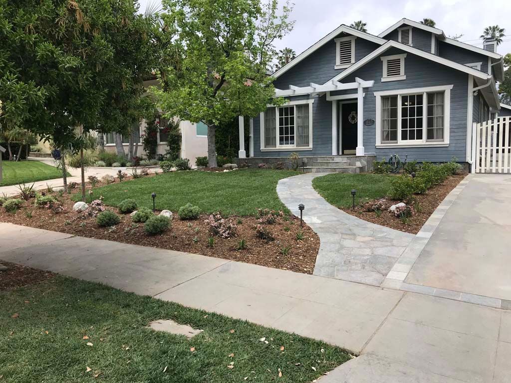 A blue house with a walkway leading to it and a lush green lawn.