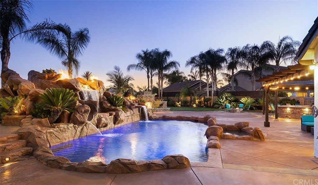 A large swimming pool with a waterfall in the backyard of a house.