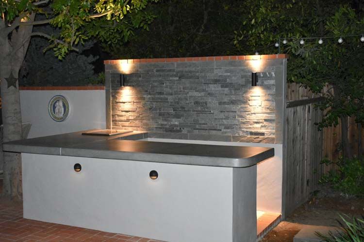 A kitchen with a brick wall and a stainless steel counter top is lit up at night.
