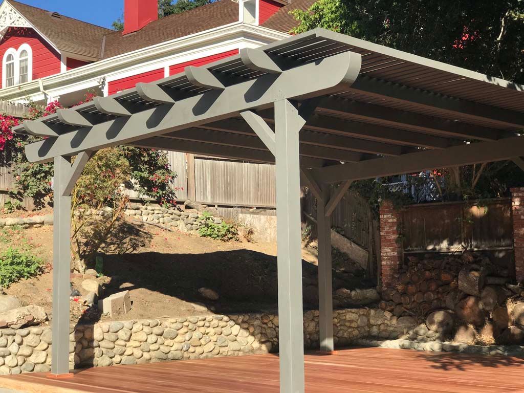 A pergola is sitting in front of a red house.