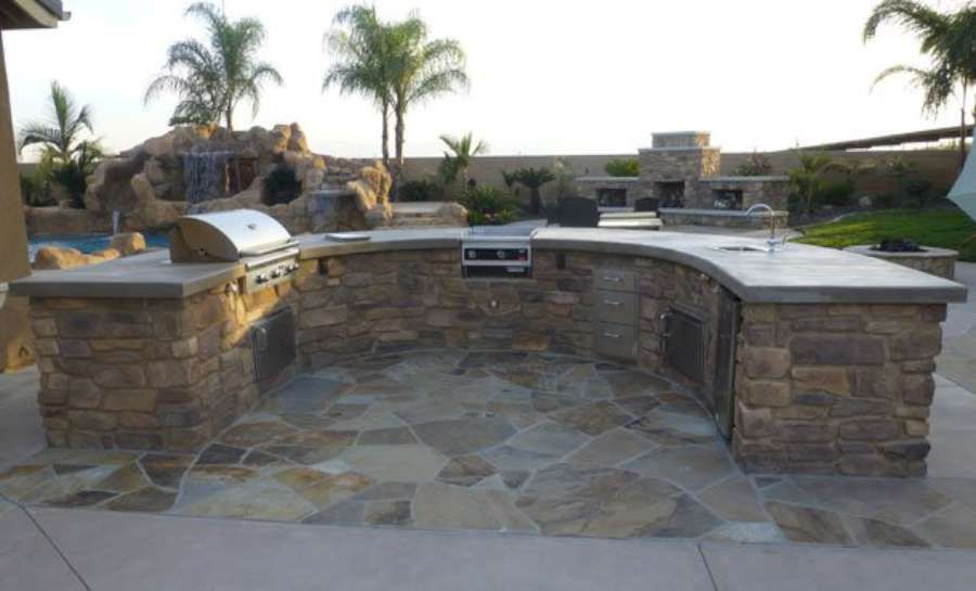 A large outdoor kitchen with a grill and a waterfall in the background