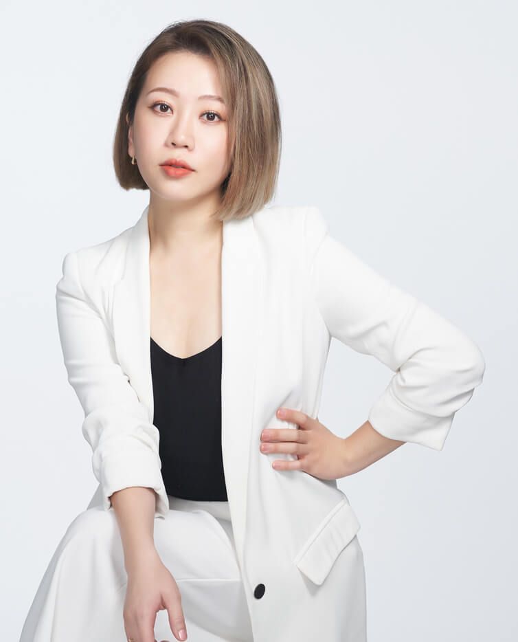 A woman in a white suit is sitting with her hands on her hips.