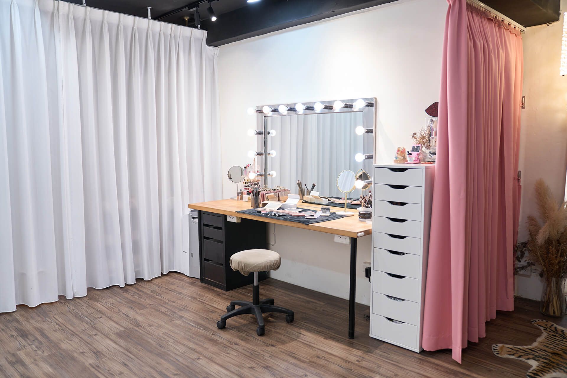 A room with a desk , chair , mirror and curtains.