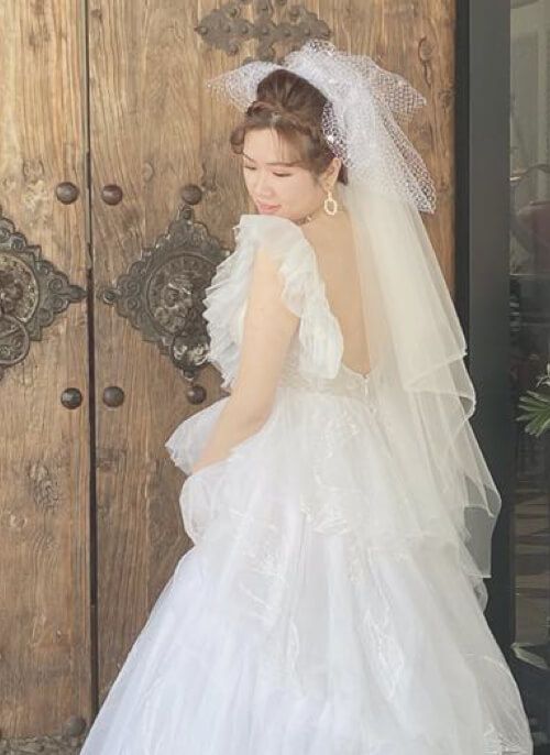 A woman in a white wedding dress and veil is standing in front of a wooden door.