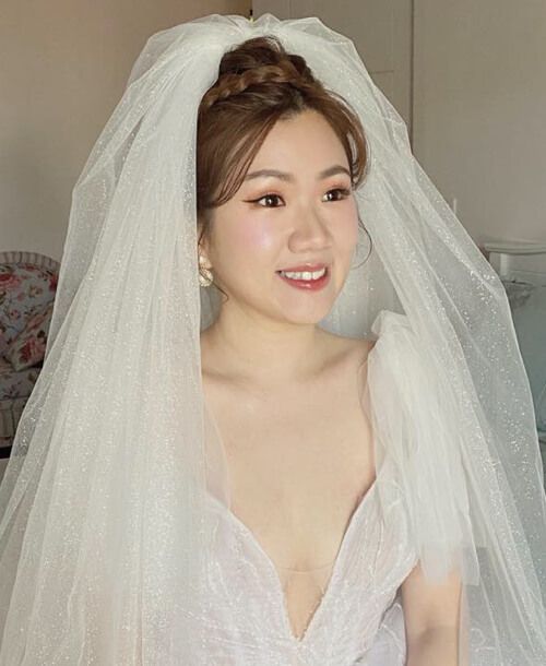 A woman in a wedding dress and veil is smiling.