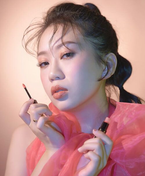 A woman in a pink dress is holding a lipstick in her hand.