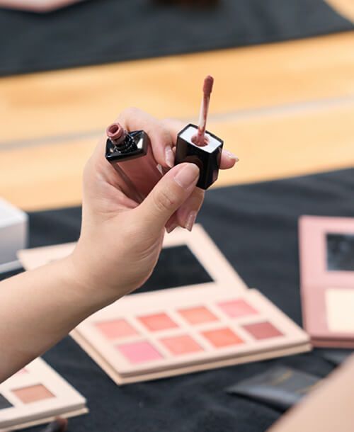 A woman is holding a bottle of lip gloss in her hand
