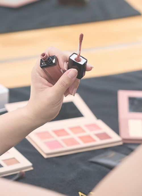 A woman is holding a bottle of lip gloss in her hand