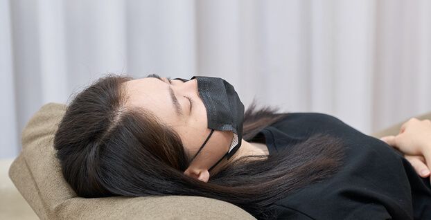 A woman wearing a black mask is sleeping on a couch.