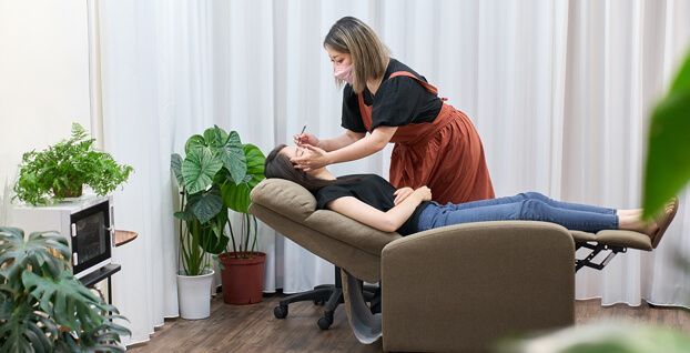A woman is laying in a chair getting her eyebrows done.